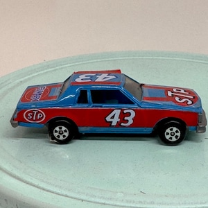 May include: A vintage toy race car in red and blue with the number 43 on the side and roof. The car has black wheels and the STP logo. A classic collectible toy.