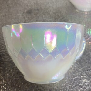 May include: A white iridescent teacup with a diamond pattern. The cup has a handle and is made of glass.