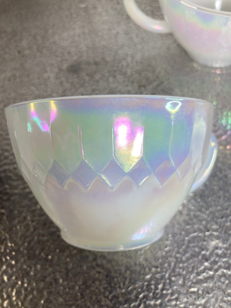 May include: A white iridescent teacup with a diamond pattern. The cup has a handle and is made of glass.