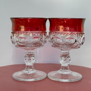 May include: Two clear glass wine goblets with a red rim. The goblets have a textured pattern and a stemmed base.