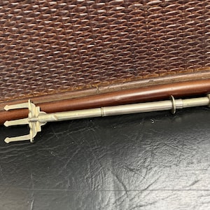 Puede incluir: Una herramienta de color plateado con tres puntas y un mango largo y delgado. La herramienta está sobre una superficie de tejido marrón.