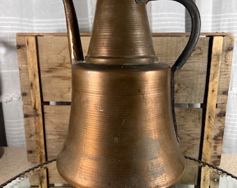 May include: A vintage copper teapot with a long spout and a black iron handle. The teapot has a rounded body and a flared base. It is sitting on a white lace doily.