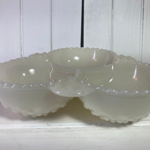 Könnte beinhalten: Eine weiße Servierschale mit drei Fächern und einem gewellten Rand. Die Schale besteht aus undurchsichtigem Glas und hat auf jeder Seite ein herzförmiges Design. Der Mittelteil ist rund.