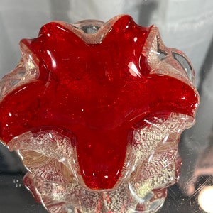 May include: A red glass ashtray with a clear, textured rim. The ashtray is shaped like a flower with five petals.