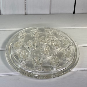 May include: A clear glass flower frog with 14 individual openings for flower stems. The frog is circular and has a raised rim.