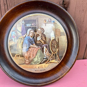 Puede incluir: Un plato de cerámica enmarcado en madera con una escena pintada de una pareja en una habitación con una rueca. El plato tiene la palabra "PERSUASION" escrita en la parte inferior.