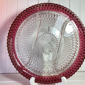 May include: A clear glass serving dish with three sections and a diamond pattern. The dish has a deep pink rim.
