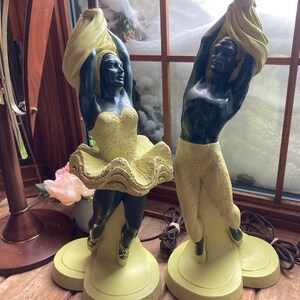 Peut inclure: Une paire de lampes de table vintage représentant des figures sculptées de danseurs en vert et noir. Les figures sont posées de manière dynamique et expressive, l'un des danseurs tenant un tissu fluide. Les lampes sont sur des bases vertes.