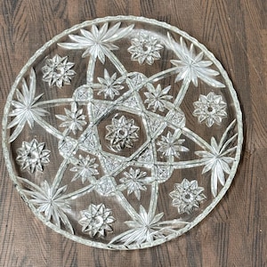 May include: A clear glass serving plate with a starburst design. The plate has a raised centre and a scalloped edge.