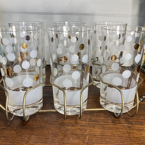 May include: Set of six clear glass highball glasses with a white and gold polka dot pattern. The glasses are in a metal holder with a black and gold design.