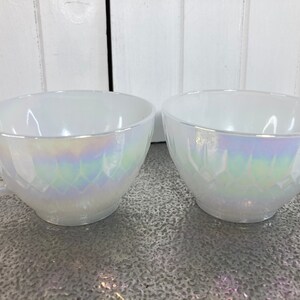 May include: Two white iridescent glass teacups with a diamond pattern. The cups have a handle on the left side.