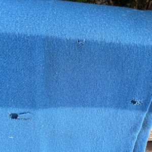 Op de afbeelding: Een blauwe deken met drie kleine gaten erin. De deken is dubbelgevouwen en ligt op een houten oppervlak.