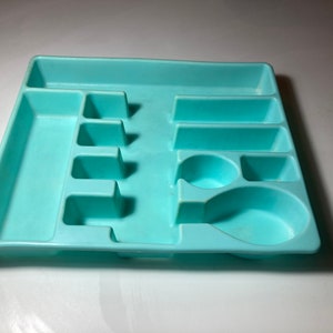 Puede incluir: Un escurridor de cubiertos de plástico azul claro con múltiples compartimentos para organizar los cubiertos. El escurridor tiene un compartimento grande para cucharas y compartimentos más pequeños para tenedores y cuchillos.