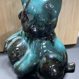 Może przedstawiać: Ceramiczna figurka kota w szkliwie turkusowym i czarnym. Kot siedzi z łapami schowanymi pod ciałem.