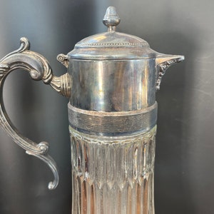 May include: A silver pitcher with a decorative handle and a glass body with a textured design.