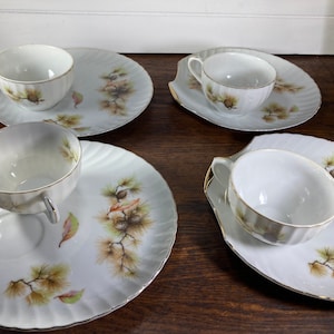 Peut inclure: Ensemble de quatre tasses à thé et soucoupes blanches avec un motif de pin. Chaque soucoupe a une petite assiette attachée pour les collations.