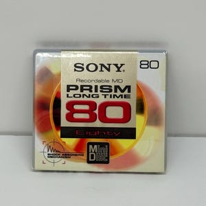 Könnte beinhalten: Quadratische Verpackung für eine Sony MiniDisc. Die Verpackung hat einen weißen Hintergrund mit dem Sony-Logo und den Worten "Recordable MD PRISM LONG TIME". Die Zahl "80" ist prominent in Rot dargestellt, darunter das Wort "Eighty".