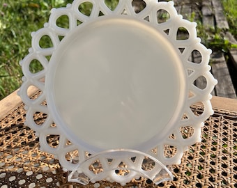 May include: A white milk glass plate with a delicate lace-like edge. The plate is round and has a smooth surface.