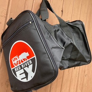 May include: Black duffel bag with a red and white logo that says "Red River EX" and a white silhouette of a buffalo pulling a wagon.
