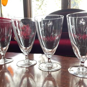 May include: Four clear glass drinking glasses with a star-shaped pattern etched into the glass. The glasses are sitting on a wooden table.