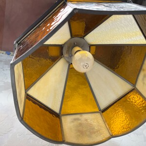 Puede incluir: Una l&aacute;mpara de techo de cristal emplomado con un dise&ntilde;o geom&eacute;trico. La l&aacute;mpara tiene un marco de metal marr&oacute;n y paneles de vidrio transparentes y &aacute;mbar.