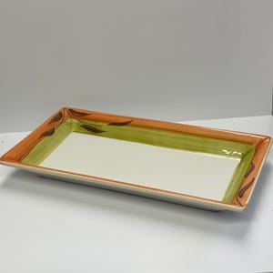 May include: Rectangular ceramic serving tray with a cream-coloured interior. The tray's border features a design of orange and green stripes, with brown leaf accents at the corners. The tray is designed for serving food.