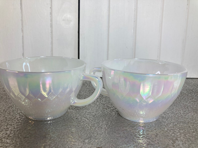 May include: Two white iridescent teacups with a diamond pattern. The cups are made of glass and have a glossy finish.