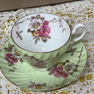 May include: A vintage teacup and saucer set with a green and white floral pattern. The cup and saucer have a gold trim.