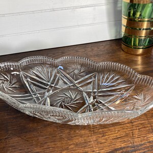 May include: A clear glass serving dish with a scalloped edge and intricate cut-glass design. The dish is oval shaped and has a delicate, elegant appearance.
