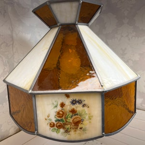 Puede incluir: Una pantalla de l&aacute;mpara de vidrio emplomado con un dise&ntilde;o floral. La pantalla est&aacute; hecha de vidrio transparente y &aacute;mbar y presenta un dise&ntilde;o floral con una cesta de flores. La pantalla tiene forma octogonal y tiene un marco de metal plateado.