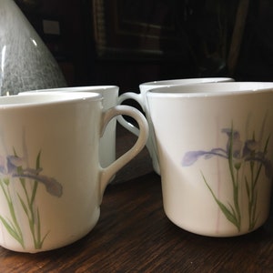 May include: Set of four white ceramic mugs with a floral design featuring purple irises and green leaves.