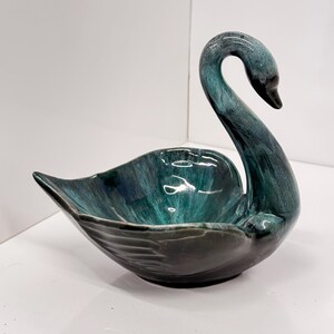 May include: A teal and green glazed ceramic swan shaped dish. The swan's neck is curved and the dish is wide and shallow.