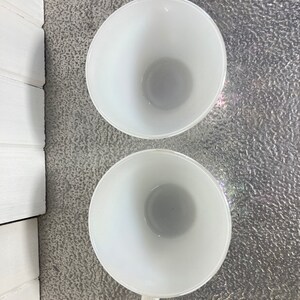 May include: Two white ceramic mugs with handles. The mugs are empty and viewed from above.