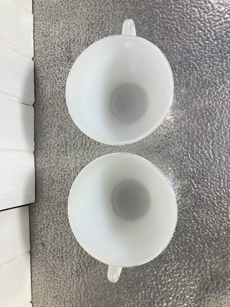 May include: Two white ceramic mugs with handles. The mugs are empty and viewed from above.