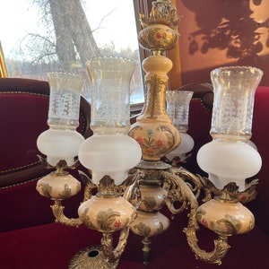 May include: A gold chandelier with six lights. The chandelier has a floral design with white and gold accents. The lights are frosted glass.