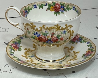 May include: A vintage teacup and saucer set with a floral pattern and gold accents. The cup and saucer are white with a delicate floral design in shades of pink, red, blue, and yellow. The gold accents are intricate and add a touch of elegance to the set.