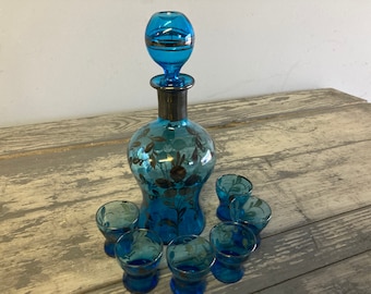 May include: A set of six blue glass shot glasses with silver floral designs and a matching blue glass decanter with a silver stopper.