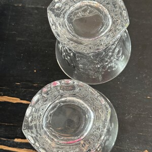 以下が含まれることがあります： 2つの透明なガラス製のタンブラー。表面は気泡のようなテクスチャで装飾されています。タンブラーは空で、暗い木製の表面の上に置かれています。