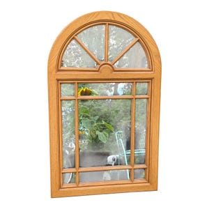 May include: A wooden arched window frame with multiple panes. The frame is a light brown colour. The window is divided into rectangular and triangular sections. A sunflower and greenery are visible through the glass.