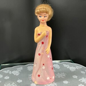 May include: A vintage porcelain doll figurine with blonde hair and blue eyes. The doll is wearing a pink dress with white and red polka dots.