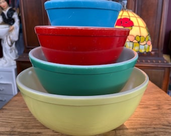 May include: A set of four vintage Pyrex mixing bowls in yellow, green, red, and blue. The bowls are nested inside each other.