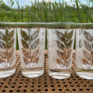 Könnte beinhalten: Set aus vier gefrosteten Gläsern mit einem Blattgold-Design. Die Gläser sind klar mit einer weißen, mattierten Oberfläche und Blattgold-Akzenten.