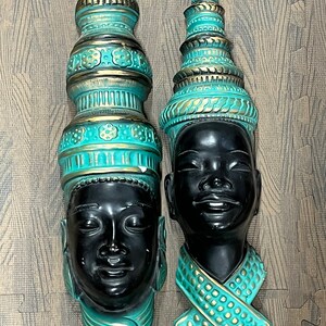 Peut inclure: Deux sculptures murales décoratives en plâtre ou en céramique représentant des visages humains avec des coiffures élaborées en turquoise et or.