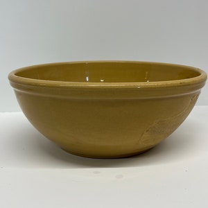 May include: A large, yellow ceramic mixing bowl. The bowl has a smooth, rounded interior and a slightly flared rim.