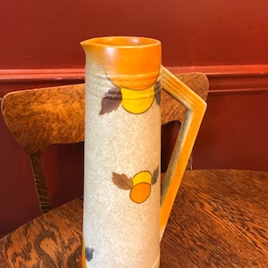 Könnte beinhalten: Eine hohe, keramische Kanne mit einem braunen, orangefarbenen und gelben geometrischen Muster. Die Kanne hat eine breite Öffnung und einen Henkel.