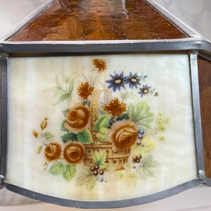 Puede incluir: Una pantalla de l&aacute;mpara de vidrio tintado con un dise&ntilde;o floral. La pantalla est&aacute; hecha de vidrio transparente con un borde marr&oacute;n y un centro blanco. El dise&ntilde;o floral presenta una cesta de flores, incluyendo rosas, margaritas y bayas.