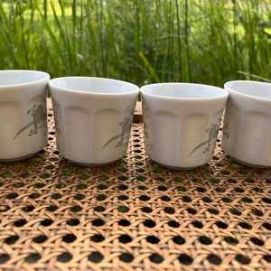 May include: Four white ceramic cups with a floral design. The cups are sitting on a woven wicker surface.