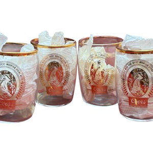 Puede incluir: Cuatro vasos transparentes con bordes dorados y un logotipo rojo y dorado con una cascada y la palabra "Coors". Cada vaso está lleno de papel de seda blanco.