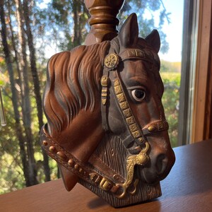 Peut inclure: Une sculpture de tête de cheval en brun et noir avec des accents dorés. Le cheval porte une bride avec un mors et une sangle décorative. La sculpture est faite d'un matériau texturé et a un aspect réaliste.