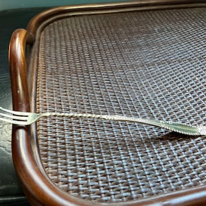 May include: A silver fork with a twisted handle rests on a brown wicker tray.